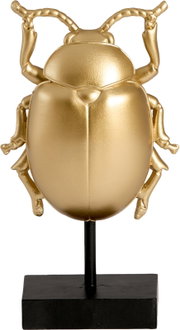 Vooraanzicht van een decoratieve goudkleurige kever op een zwarte metalen standaard tegen een witte achtergrond