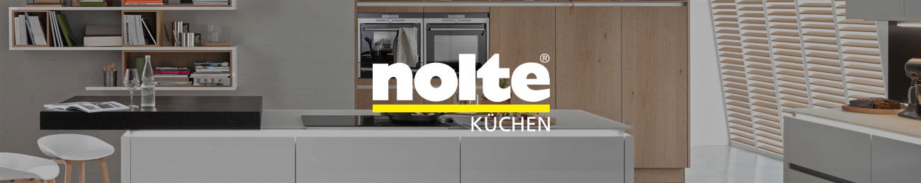 Das Bild zeigt eine moderne Küche von Nolte. In der Mitte steht eine weiße Kücheninsel mit einer schwarzen Arbeitsplatte. Im Hintergrund sind Holzschränke und eingebaute Geräte zu sehen. Links gibt es offene Regale mit Büchern und Gläsern.