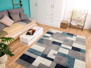 Moderner Frisé-Teppich in geometrischem Design mit Grautönen und Blautönen, in einem hellen Wohnzimmer mit Holzboden, Sofa und Dekorationen, aus der Vogelperspektive betrachtet.