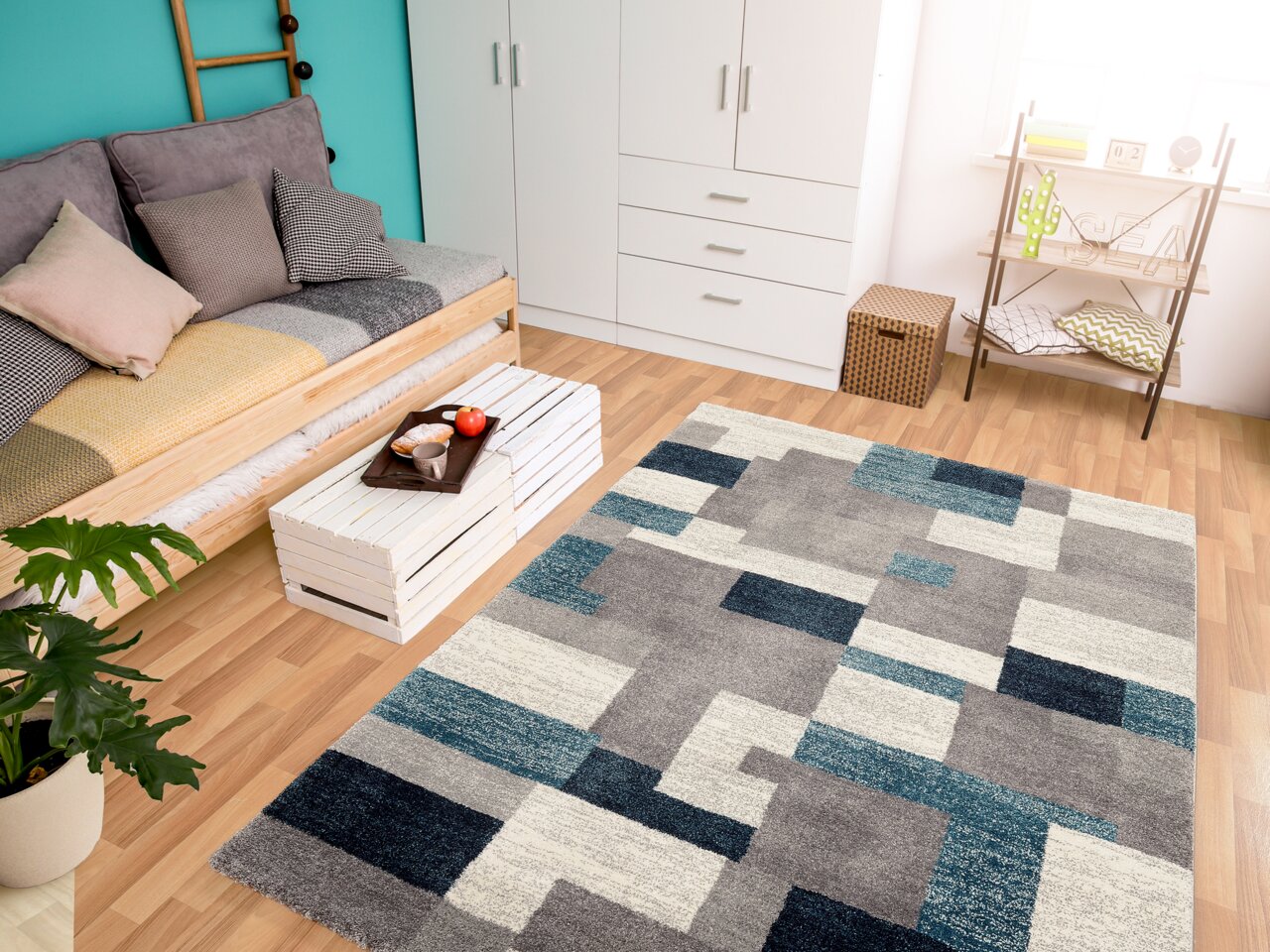 Moderner Frisé-Teppich in geometrischem Design mit Grautönen und Blautönen, in einem hellen Wohnzimmer mit Holzboden, Sofa und Dekorationen, aus der Vogelperspektive betrachtet.