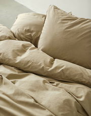 Beige Bettwäsche-Set in Nahaufnahme, bestehend aus einem Kissen und einer Decke, auf einem Bett arrangiert.