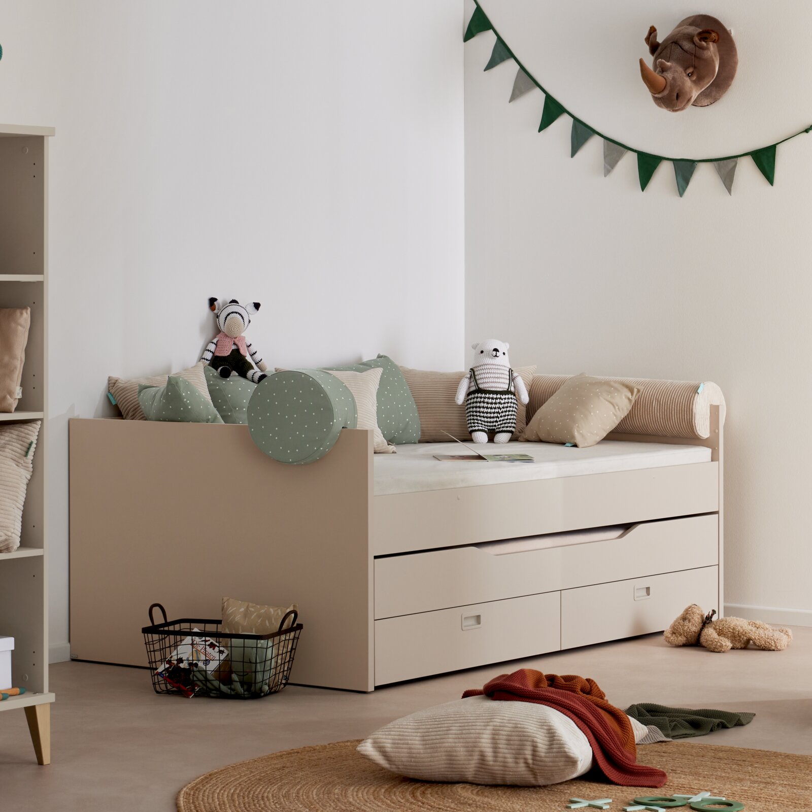 Kinderzimmer mit beigem Tagesbett mit Ausziehbett und Schubladen, dekoriert mit Kissen und Stofftieren, seitliche Perspektive