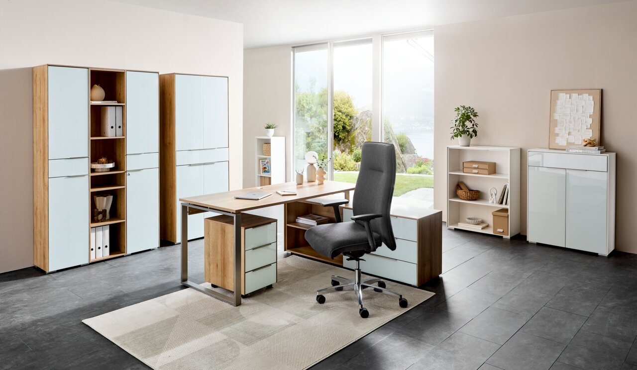 Voleo Aktenschrank NEVADA Moderne Büromöbelkombination mit Schreibtisch, Rollcontainer und Aktenschränken in einem hellen Raum mit Blick auf den Garten, aus der Perspektive von vorne.