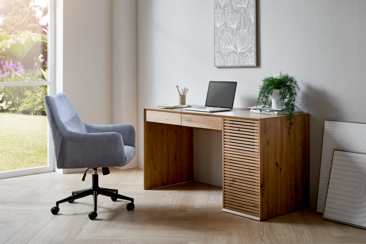 Moderner Schreibtisch aus Holz mit Schubladen und Lamellen-Design, seitliche Perspektive, neben einem Fenster mit Blick ins Grüne.