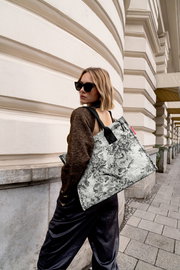 Frau mit Sonnenbrille trägt eine stilvolle Einkaufstasche mit schwarz-weißem Muster über der Schulter, seitliche Perspektive.