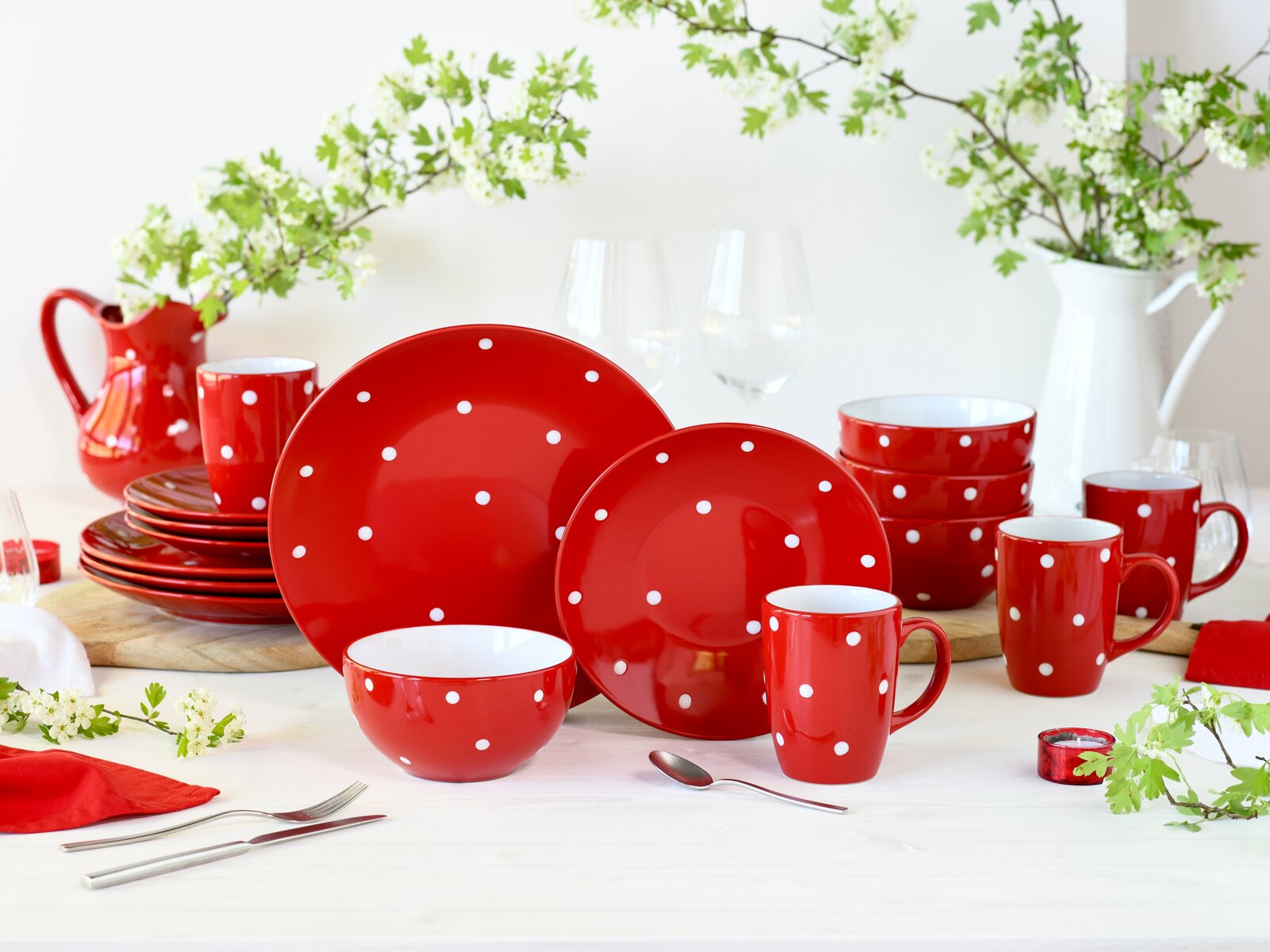 Rotes Geschirr-Set mit weißen Punkten (Teller, Schalen, Tassen und Krug) dekorativ auf einem Tisch arrangiert, frontale Perspektive auf die Produkte