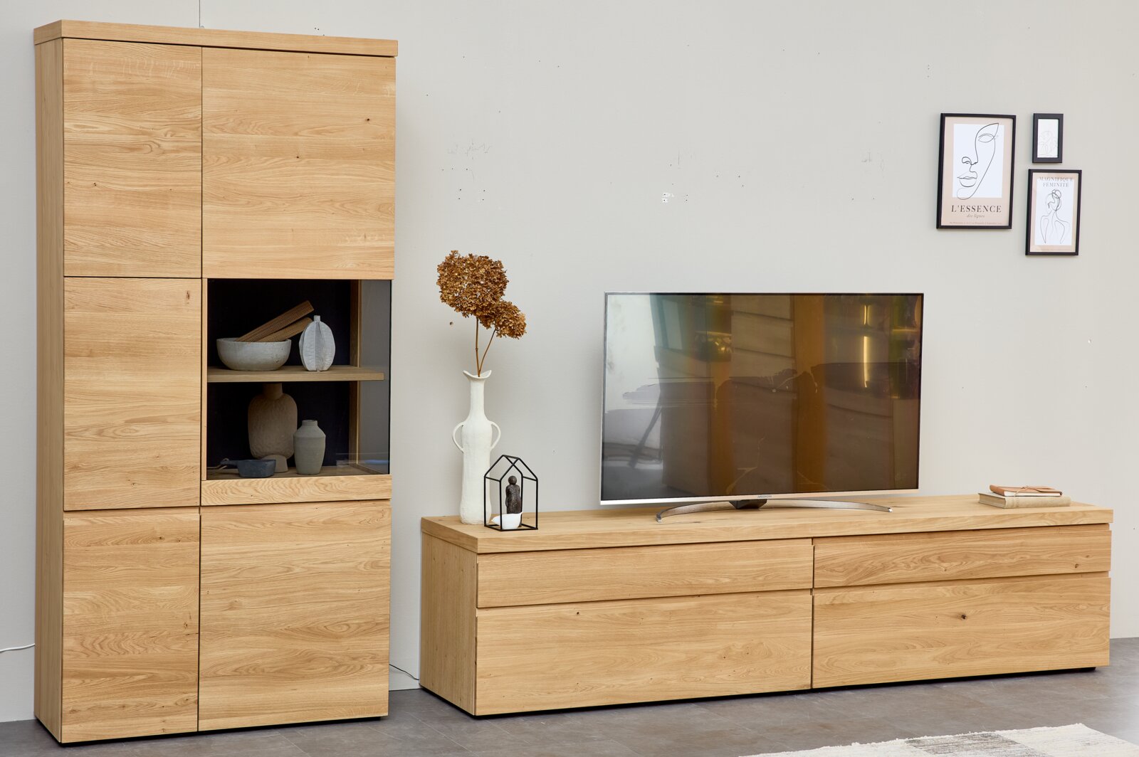 Moderne Wohnwand aus naturbelassen wirkendem Eichenholz mit hoher Vitrine, offenen Dekofächern und breitem TV-Lowboard, in leicht seitlicher Frontalansicht.