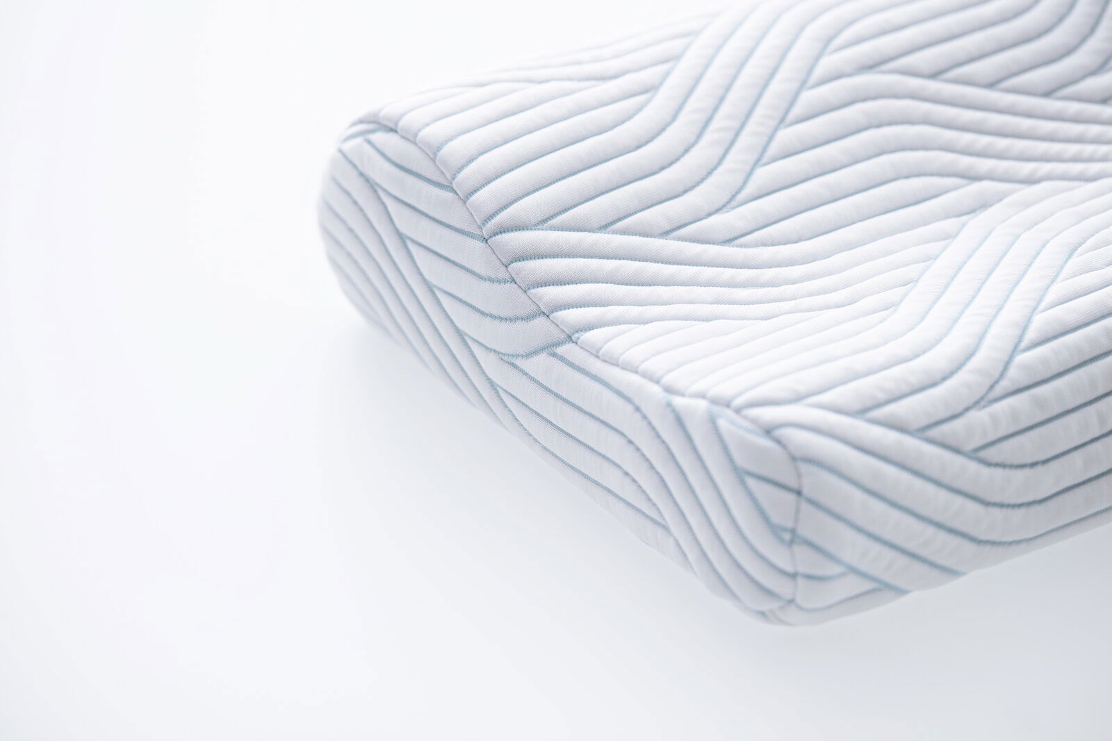 Nahaufnahme eines ergonomischen Schlafkissens mit gestepptem Bezug und wellenförmigem Muster, perspektivisch von der Seite aufgenommen.