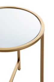 Runder Beistelltisch mit goldfarbenem Metallrahmen und Spiegelglasplatte, Detailansicht von schräg oben auf die Tischkante und ein Bein vor weißem Hintergrund