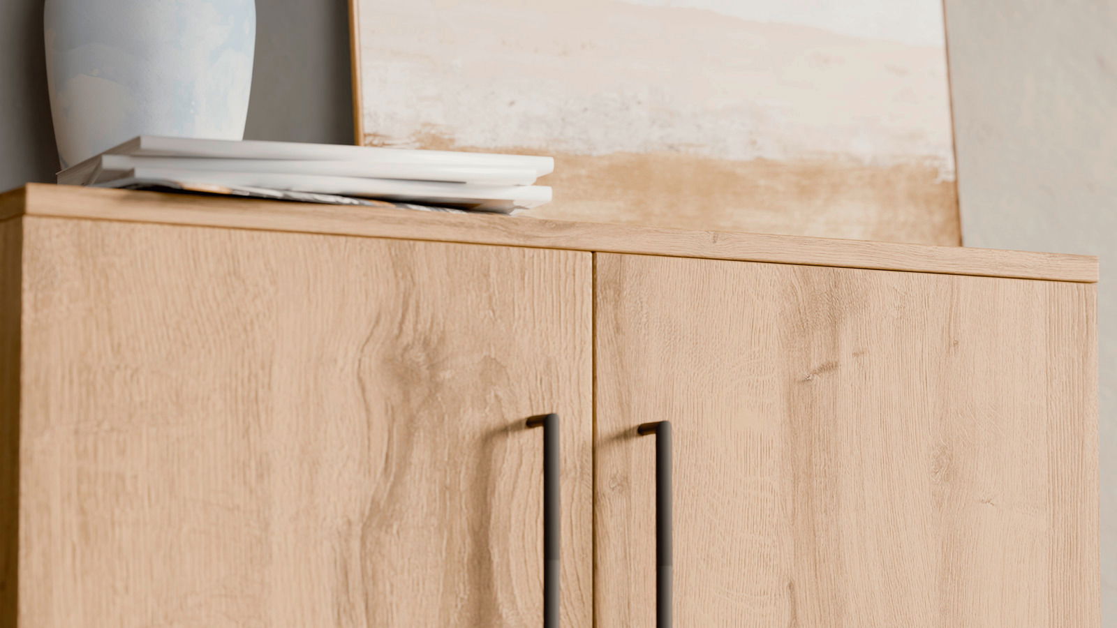 Nahaufnahme eines Schuhschranks aus hellem Holz mit schwarzen Griffen, von vorne betrachtet. Obenauf stehen ein blauer Keramikvase und einige Bücher.
