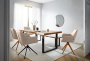 Moderner Essbereich mit einem großen Holztisch und mehreren beigen Armlehnstühlen auf einem hellen Teppich, seitliche Perspektive.