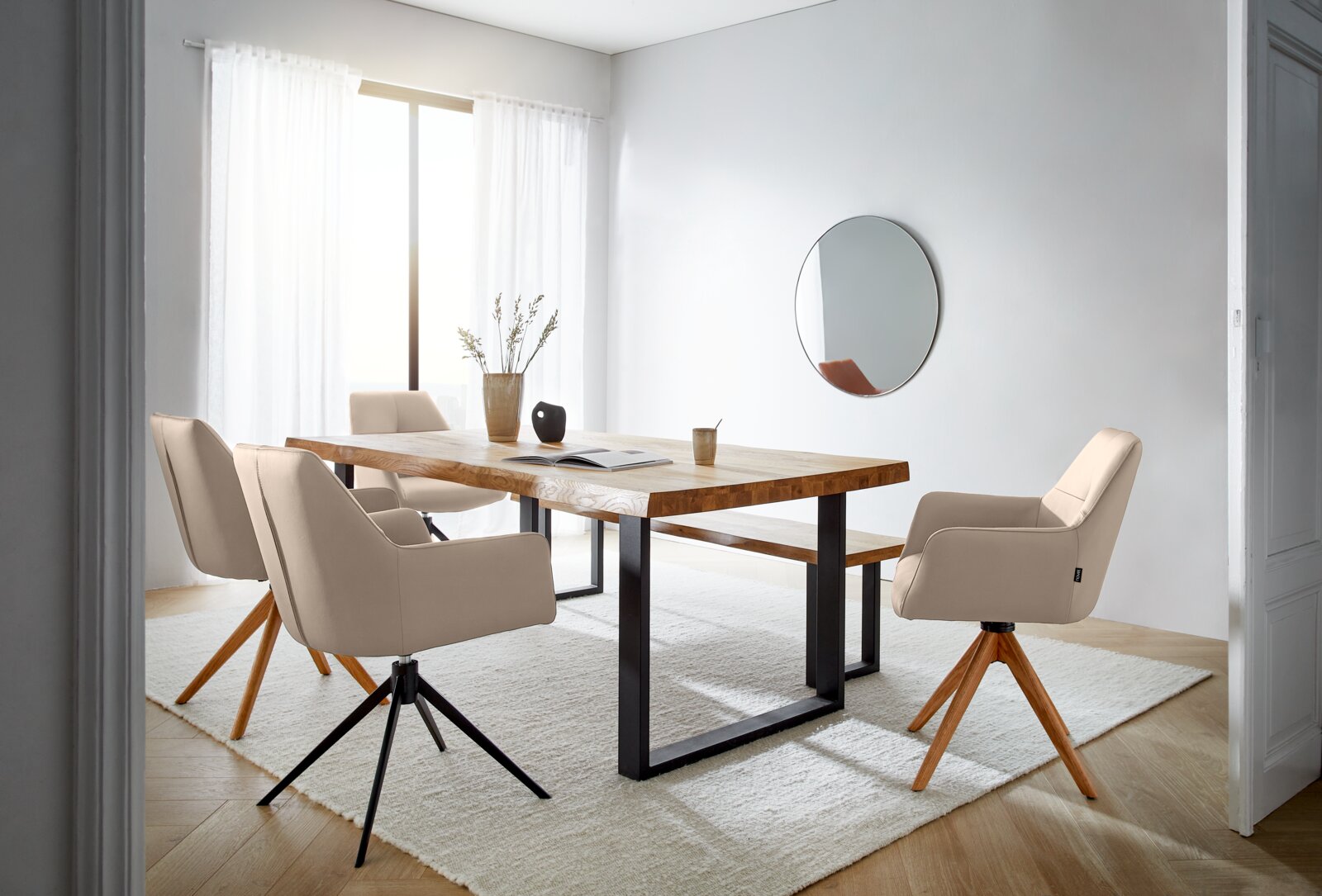 Moderner Essbereich mit einem großen Holztisch und mehreren beigen Armlehnstühlen auf einem hellen Teppich, seitliche Perspektive.