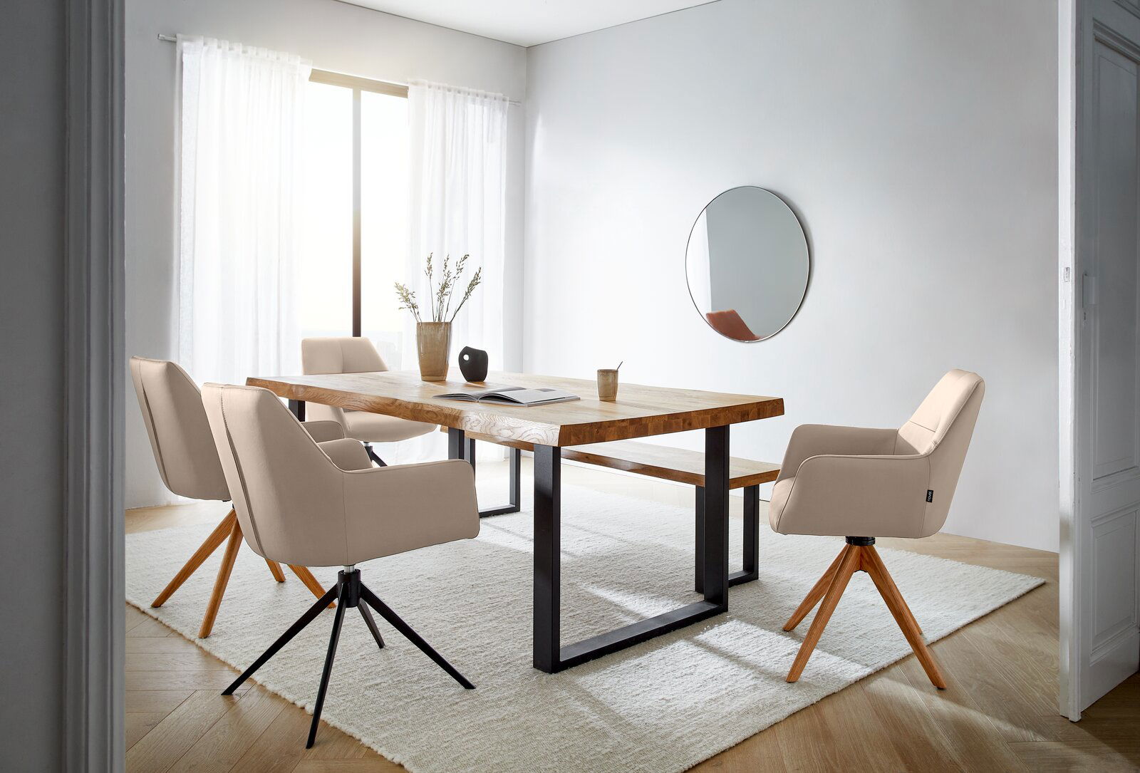 Moderner Essbereich mit einem großen Holztisch und mehreren beigen Armlehnstühlen auf einem hellen Teppich, seitliche Perspektive.