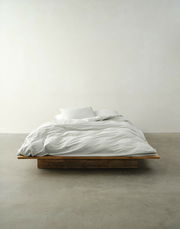 Bett mit weißer Bettwäsche in minimalistischer Umgebung, Vorderansicht