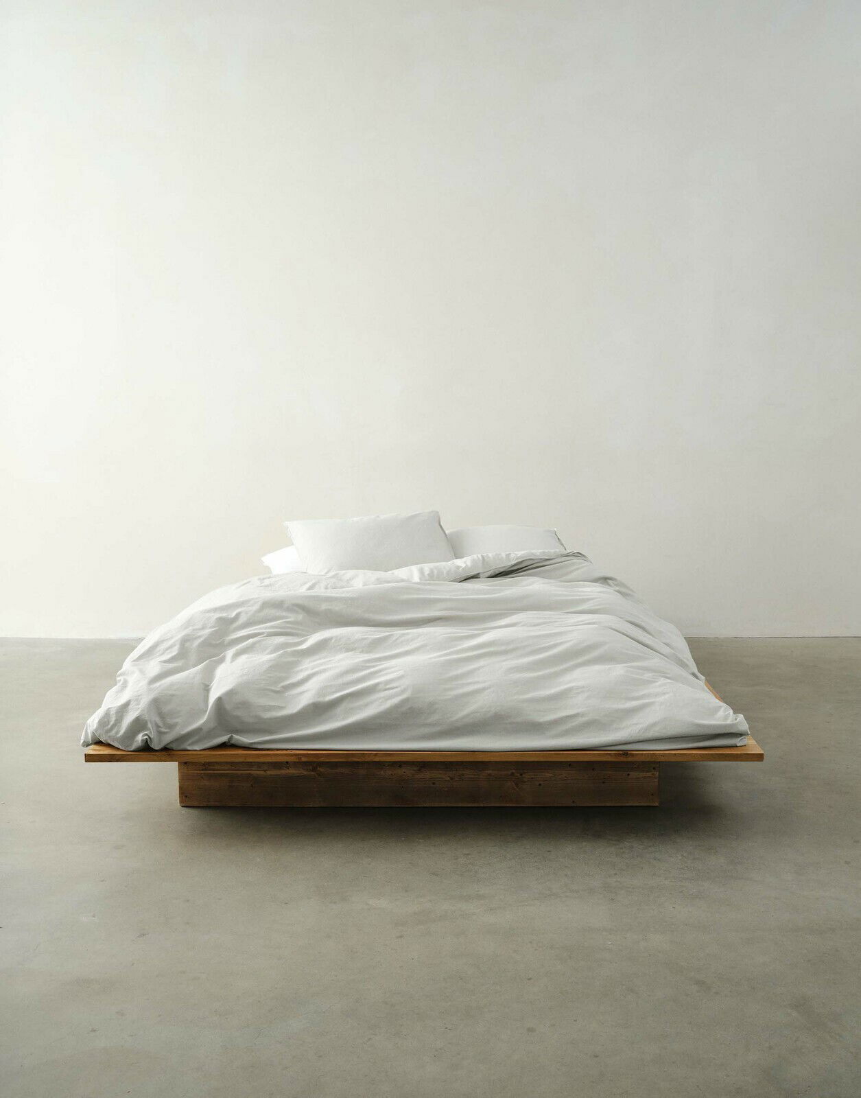 Bett mit weißer Bettwäsche in minimalistischer Umgebung, Vorderansicht