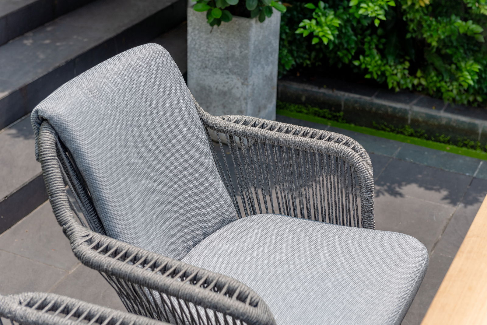 Grauer Armlehnstuhl mit geflochtenen Seil-Details, seitliche Perspektive im Freien.