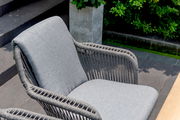 Grauer Armlehnstuhl mit geflochtenen Seil-Details, seitliche Perspektive im Freien.
