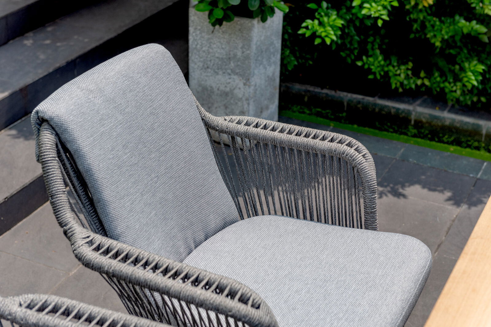 Grauer Armlehnstuhl mit geflochtenen Seil-Details, seitliche Perspektive im Freien.