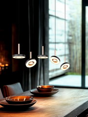 Moderne LED hanglamp met vijf ronde, ringvormige pendels in zwart met warmwitte lichtkringen boven een houten eettafel, zijaanzicht in interieursetting