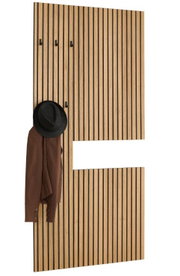 Moderne Garderobenpaneel aus hellem Holz mit vertikalen schwarzen Lamellen, mehreren schwarzen Haken und weißem Ablagefach, mit aufgehängtem braunem Mantel und schwarzem Hut; Ansicht schräg von vorne.