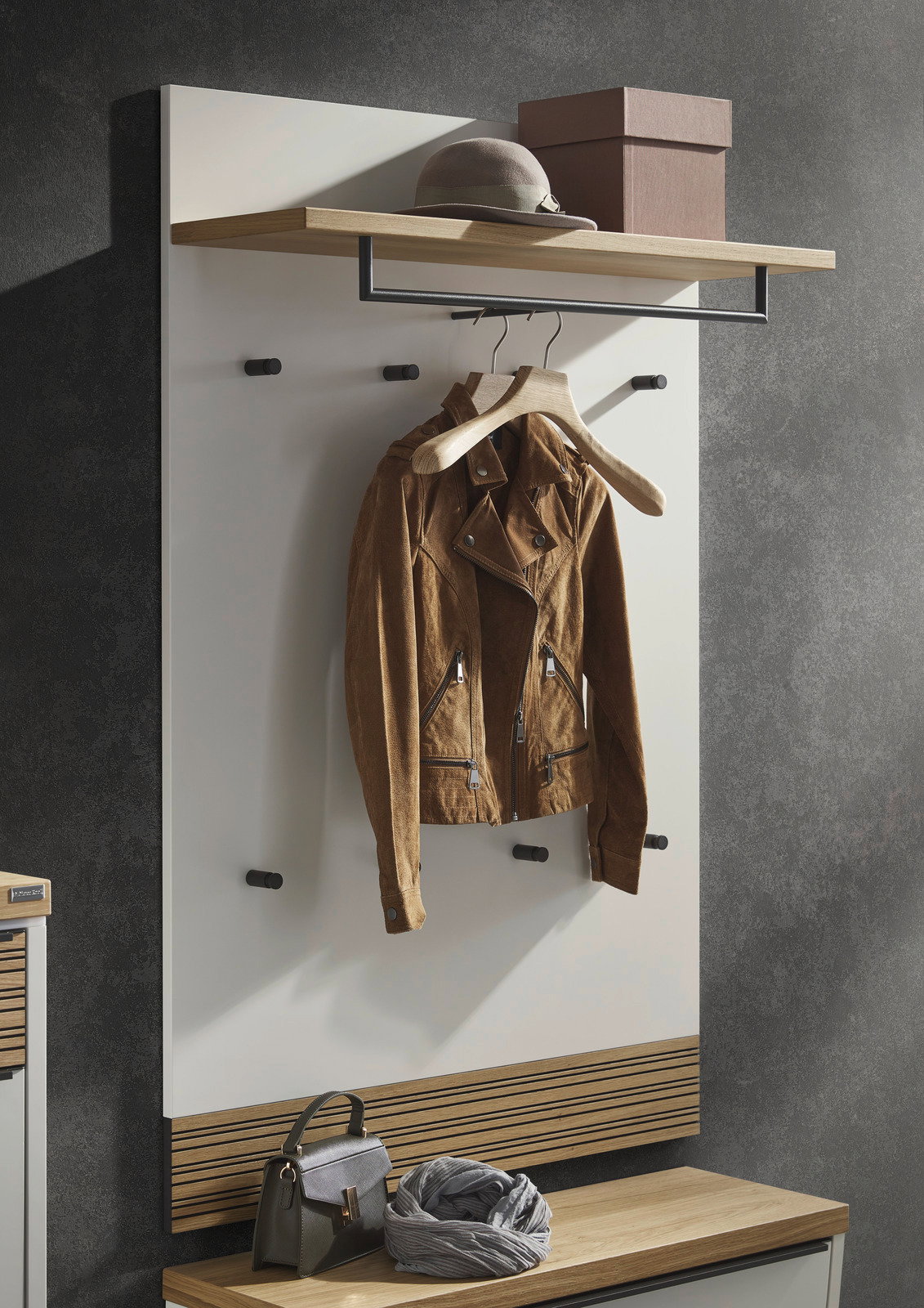Garderobenpaneel in moderner Optik mit Haken, Ablage und Kleiderstange, frontal fotografiert. Eine Jacke hängt an einem Kleiderbügel, darüber ein Hut und eine Box auf der Ablage.