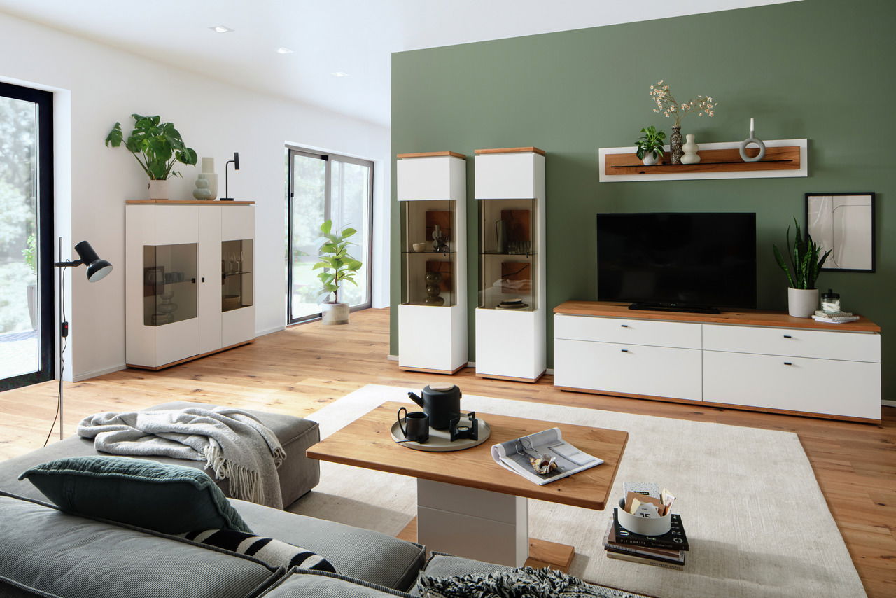 Modernes Wohnzimmer mit Wandboard, das über einem Fernseher an einer grünen Wand montiert ist. Perspektive von der Seite, die den gesamten Raum zeigt.