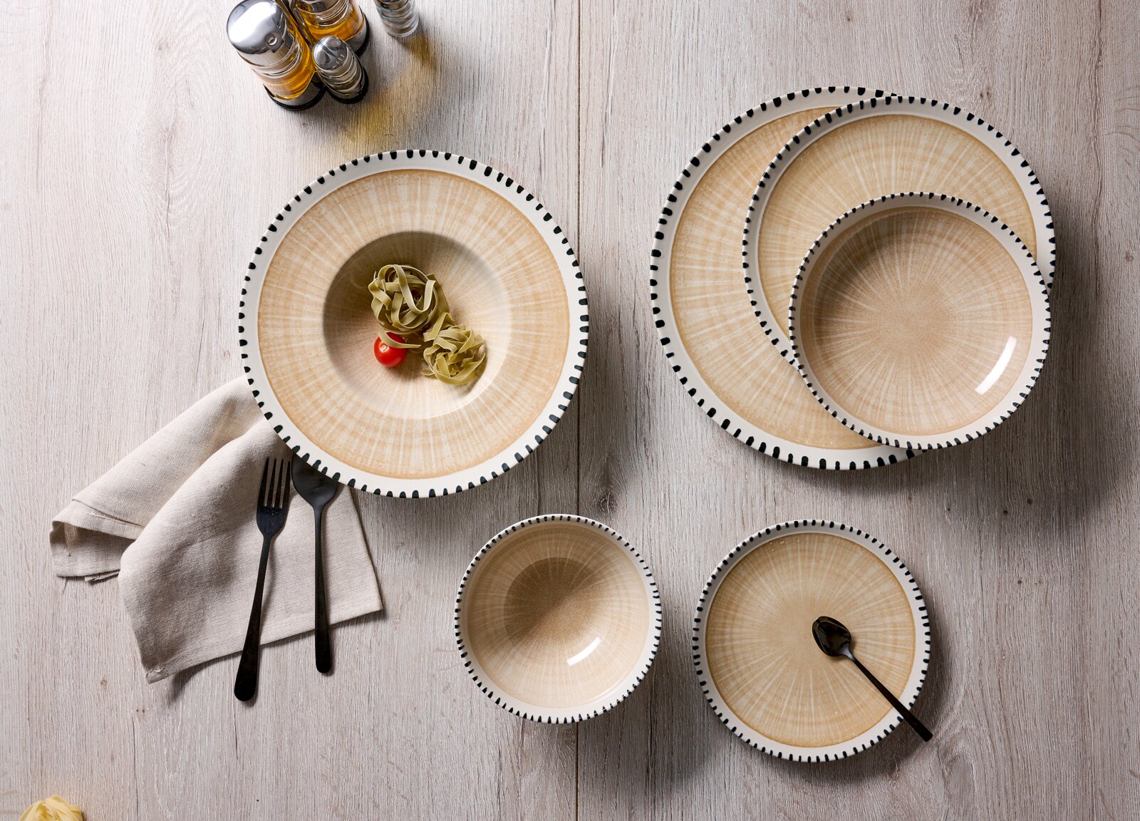 Van bovenaf gefotografeerd beige servies met een subtiel straalpatroon en decoratieve zwarte streepjes langs de rand, stijlvol gedekt op een lichte houten tafel.