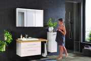 Moderne Badkombination mit weißem Waschtisch, Spiegelschrank und seitlichem Schrank, fotografiert aus einer frontalen Perspektive. Eine Frau steht daneben, umgeben von Pflanzen und einer Dusche im Hintergrund.