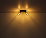 Zweiflammiger Strahler aus schwarzem Metall, montiert an der Decke, mit warmem Lichtschein, seitliche Perspektive.