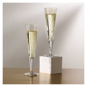 Zwei elegante Champagnergläser mit goldenen Sternenmotiven, eines auf einem weißen Sockel, aus seitlicher Perspektive fotografiert.