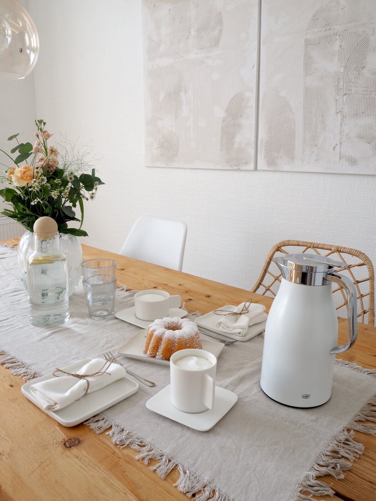 Elegante weiße Isolierkanne mit glänzendem Deckel auf einem gedeckten Tisch, seitliche Perspektive.