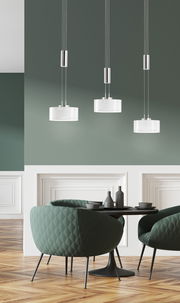 Moderne LED-Pendelleuchte mit drei Leuchten, hängend über einem stilvollen Essbereich mit grünen Sesseln und einem runden Tisch, seitliche Perspektive.