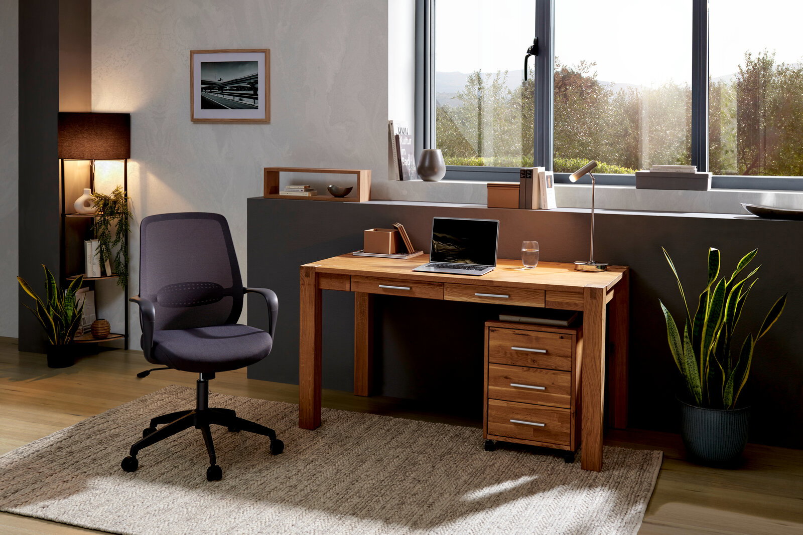 Moderner Schreibtisch aus Holz mit Schubladen, Laptop und Lampe, seitliche Perspektive