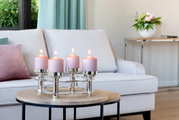 Moderne kandelaar met vier kaarsen en roze kaarsen op een ronde houten tafel, op de achtergrond een witte bank en een bloemstuk, zijaanzicht.