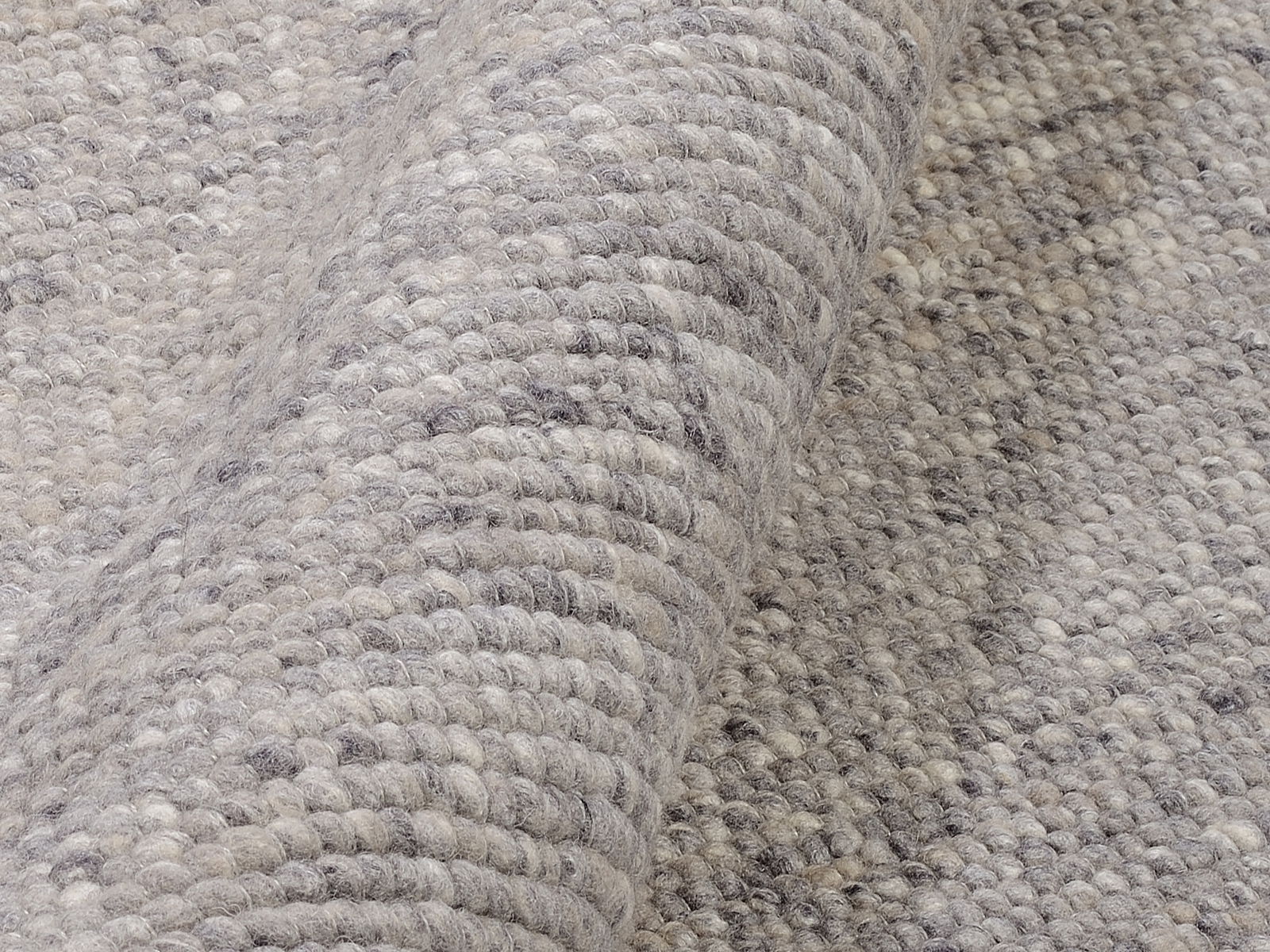 Nahaufnahme eines handgewebten Teppichs in Grautönen, der eine detaillierte Ansicht der Textur und Webart zeigt.