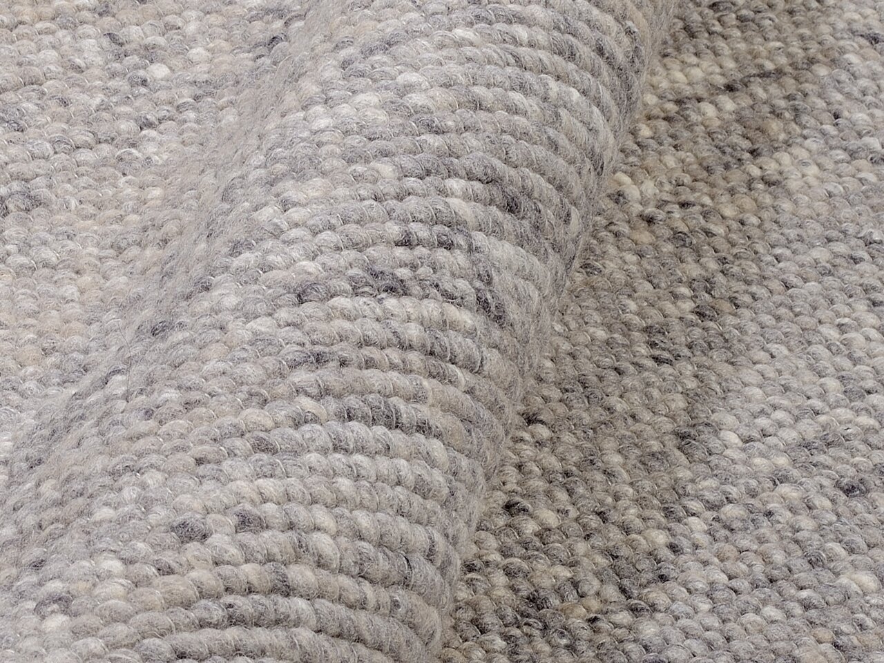 Nahaufnahme eines handgewebten Teppichs in Grautönen, der eine detaillierte Ansicht der Textur und Webart zeigt.