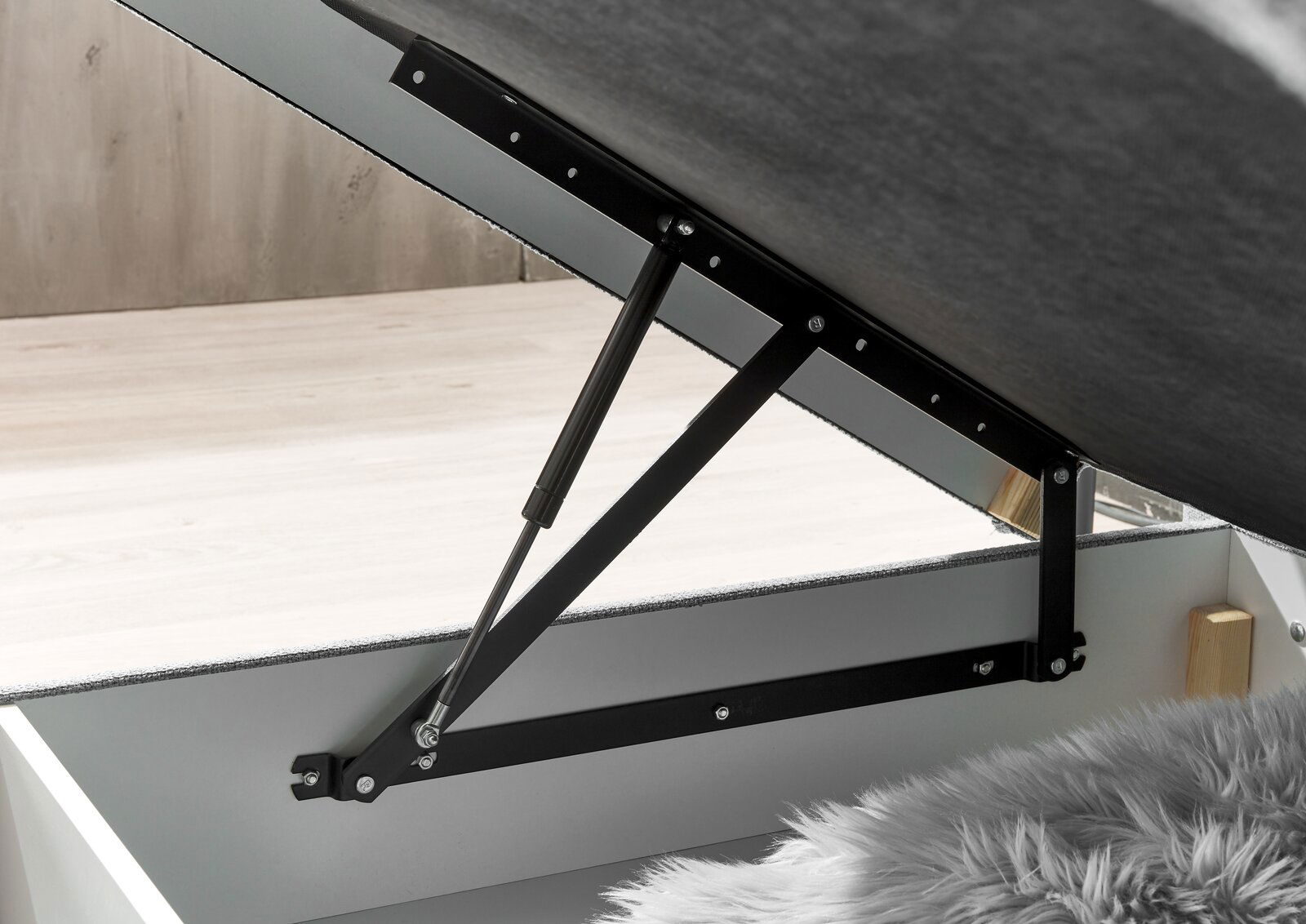 Nahaufnahme eines geöffneten Boxspringbetts mit hydraulischem Hebemechanismus, seitliche Perspektive.