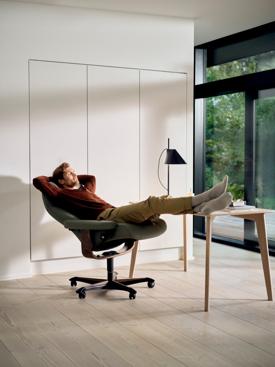 Mann entspannt sich in einem Chefsessel mit Füßen auf einem Tisch, seitliche Perspektive