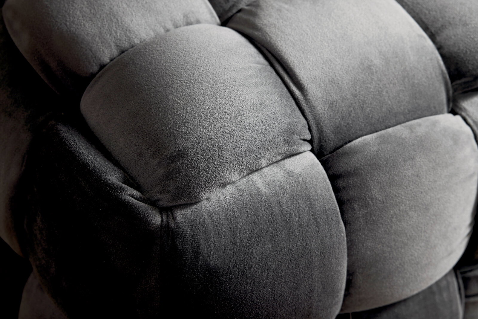 Nahaufnahme eines grauen, gepolsterten Hockers mit weicher, samtartiger Oberfläche. Perspektive von oben.