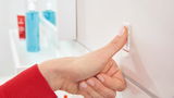 Nahaufnahme einer Hand, die einen tesa Powerstrip Haken an einer Wand befestigt. Die Perspektive zeigt die Hand von der Seite.