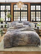 Gemütliches Schlafzimmer mit irisette Bettwäsche ZOBEL in natürlichem Design, fotografiert aus der Frontperspektive. Die Bettwäsche zeigt ein dezentes, erdiges Muster und ist auf einem stilvoll eingerichteten Bett in einem hellen Raum mit großen Fenstern 