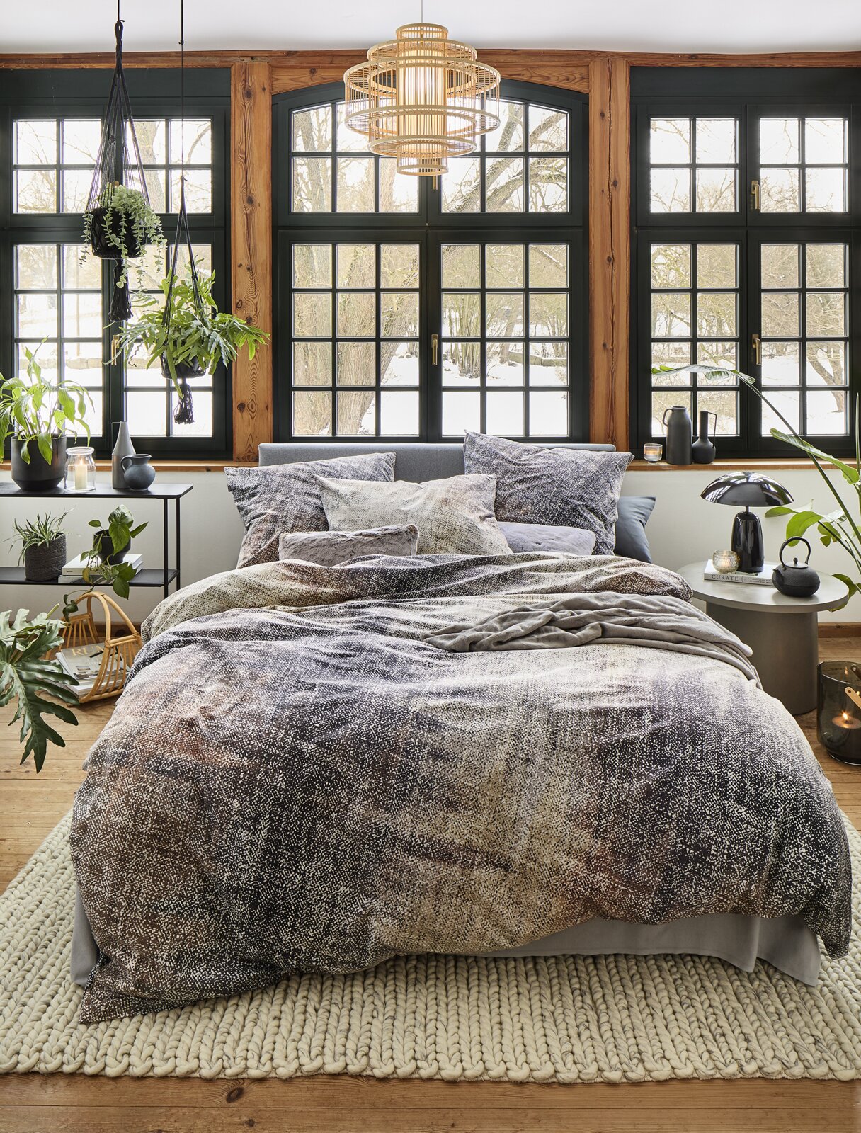 Gemütliches Schlafzimmer mit irisette Bettwäsche ZOBEL in natürlichem Design, fotografiert aus der Frontperspektive. Die Bettwäsche zeigt ein dezentes, erdiges Muster und ist auf einem stilvoll eingerichteten Bett in einem hellen Raum mit großen Fenstern