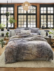 Gemütliches Schlafzimmer mit irisette Bettwäsche ZOBEL in natürlichem Design, fotografiert aus der Frontperspektive. Die Bettwäsche zeigt ein dezentes, erdiges Muster und ist auf einem stilvoll eingerichteten Bett in einem hellen Raum mit großen Fenstern 