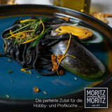 Nahaufnahme eines blauen Tellers mit schwarzer Pasta, Muscheln und Garnitur, ideal für Hobby- und Profiköche.