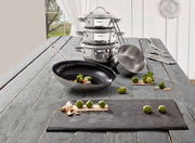 Topfset 5-tlg. aus Edelstahl, bestehend aus gestapelten Töpfen und einer Pfanne, auf einem rustikalen Holztisch mit Blick auf ein Fenster im Hintergrund.