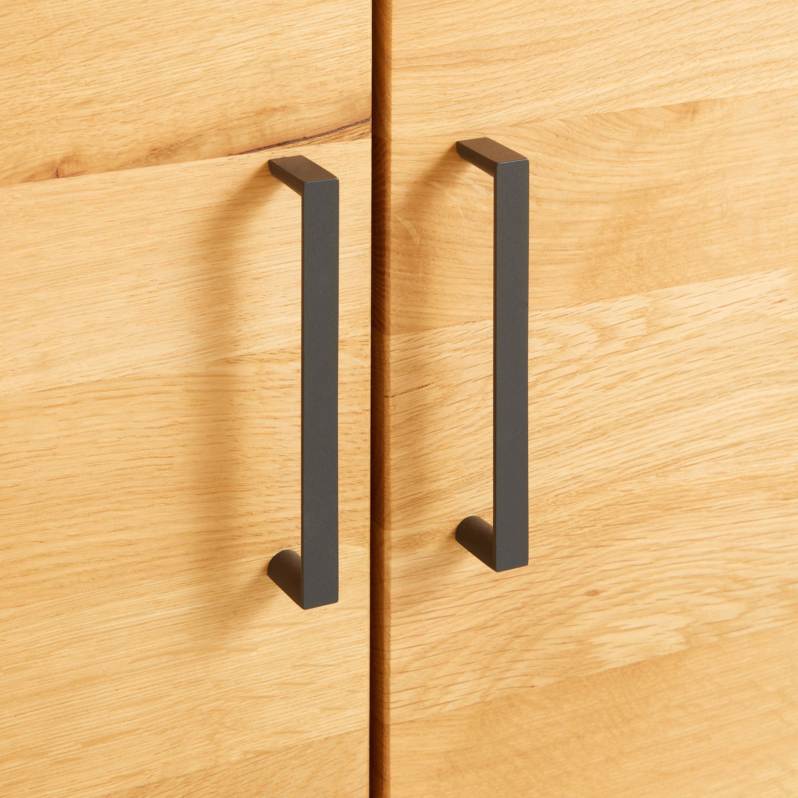 Nahaufnahme von zwei schwarzen Griffen an einer Holztür eines Regalschranks, frontal betrachtet.