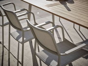 Zwei Stapelsessel aus Metall und Stoff an einem Holztisch, seitliche Perspektive