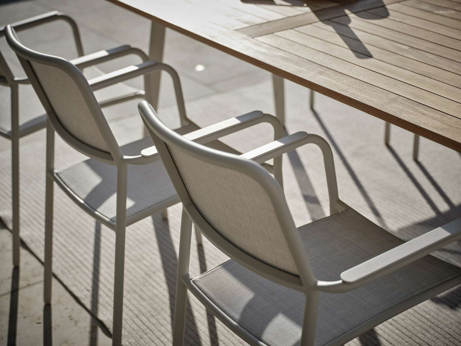 Zwei Stapelsessel aus Metall und Stoff an einem Holztisch, seitliche Perspektive