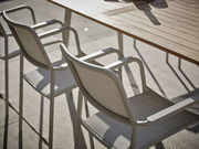 Zwei Stapelsessel aus Metall und Stoff an einem Holztisch, seitliche Perspektive