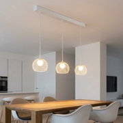 Moderne hanglamp met drie lampen, voorzien van witte, bolvormige gaaskapjes aan een lange plafondbeugel boven een eettafel; perspectief: licht van onderaf en frontaal in de ruimte